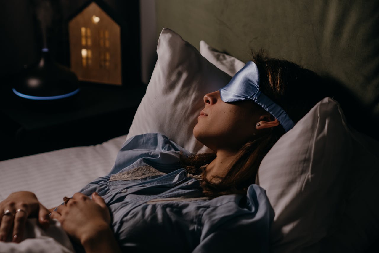 pexels photo 6541121 A woman sleeping peacefully wearing a blue eye mask in a cozy, dimly lit bedroom.