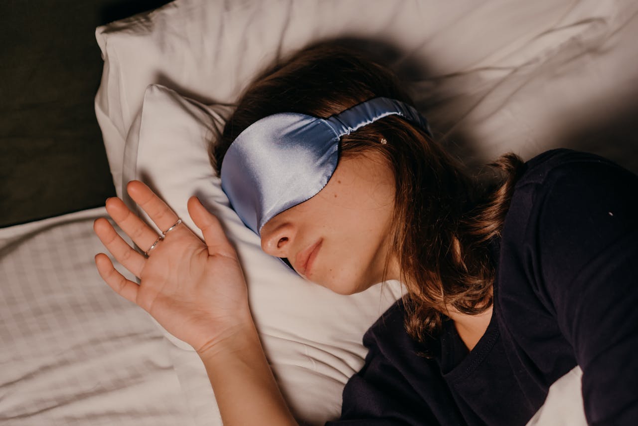 A woman rests peacefully indoors wearing a blue silk sleep mask.