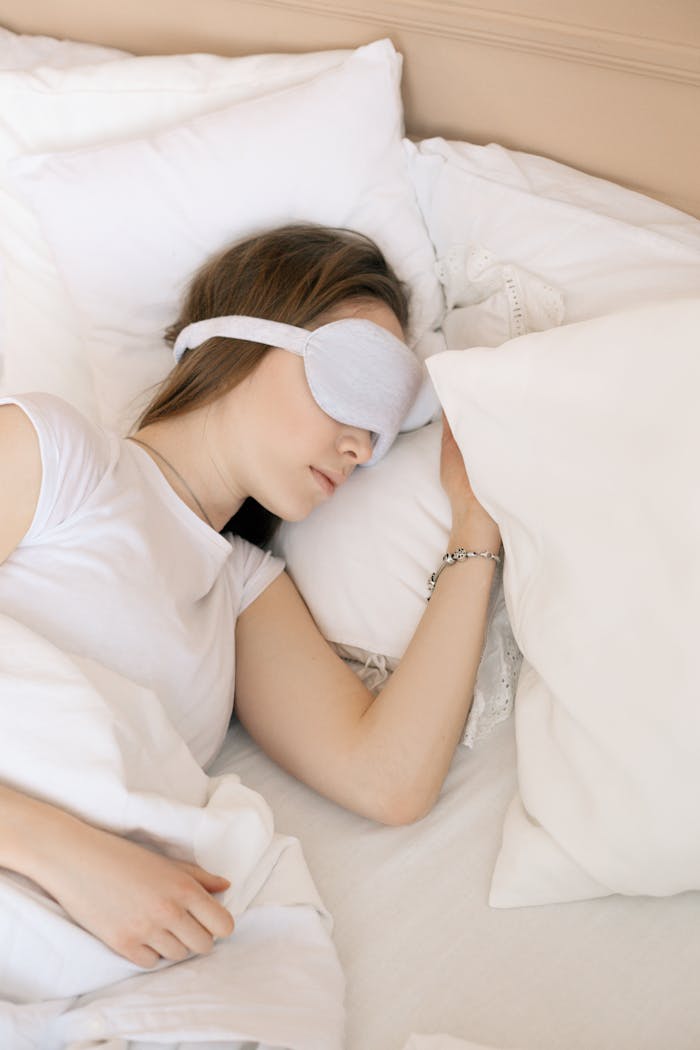 A serene scene of a woman sleeping with a white sleep mask in a cozy bed.